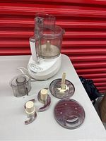 Full view of food processor base unit with attached large processing bowl, feed chute, and multiple blades and discs laid out beside it.