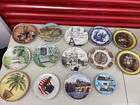 Photo showing all 14 decorative plates arranged on a white surface.