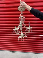 Photo showing full view of ivory chandelier held by hand with ceiling mount, leaf shaped metal arms, and hanging clear crystal droplets.