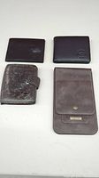 Four men's wallets of various sizes and styles laid out on a white surface.