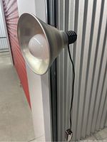 Photo showing metal reflector shade with white bulb installed, angled forward, power cord hanging down.