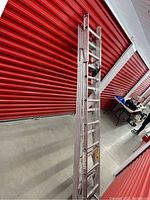 Full view of aluminum multi-section ladder leaning against a red industrial door, showing extended and nested sections.