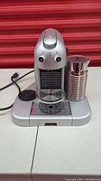Front view of silver Nespresso machine with two dials and frother at side