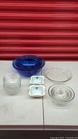 Full lot overview with all glassware pieces including nested blue bowls, clear glass pie plate, small clear bowls, and white dishes visible