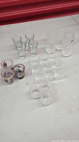 Multiple shot glasses grouped on flat surface, showing variety of sizes, shapes, and decoration including clear, etched, and painted glasses.