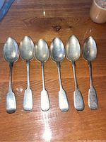 Six silver spoons laid side by side showing full set and shape