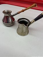 Photo showing two Turkish coffee pots side by side on a white surface with a red background