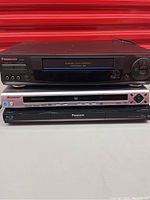 Photo of three media players stacked: Panasonic VHS player PV 96614 on top, silver Pioneer DVD player DV 588A in middle, Panasonic DM-BD35 Blu-ray player bottom.