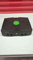 Front view of the original Xbox showing the central green logo, power and eject buttons, and four controller ports.