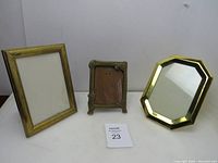 Lot of three brass picture frames on a white surface, showing the variety in shape and size.