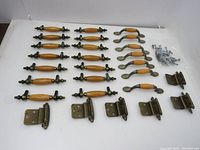 Lot contents showing 16 wood and cast metal drawer pull handles, 5 curved wood and metal handles, 5 cast metal hinges, and screws in small plastic bag on white background.