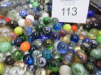 Close up of a large mixed lot of glass marbles in assorted colors and finishes including transparent, opaque, and iridescent hues.