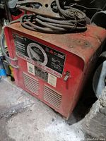 Front and angled views of red Lincoln Electric AC 225 Arc Stick Welder showing control panel with amperage dial, cables, clamp, and rusted exterior.