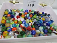 Marbles assortment in white plastic container showing many colorful marbles with different patterns and colors.