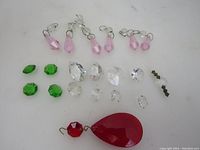 Photo showing all chandelier glass prisms on a white surface, displaying varying sizes, shapes and colors including burgundy, pink, green and clear white prisms with metal hangers.