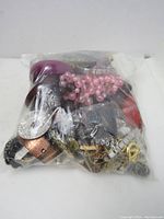 Photo of a sealed plastic bag containing a large mixed assortment of broken jewelry pieces, including metal chains, beads, and watch parts.
