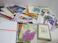 Photo showing a pile of assorted greeting cards and envelopes in various colors and designs, some with visible floral and butterfly illustrations.