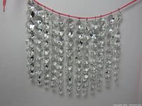 Full view of the 12 crystal strings hanging on a pink cord against a white wall.