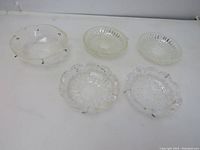 Lot of five glass chandelier bobeches arranged on a white surface, showing crystal and cut glass pieces with pins and pressed glass pieces without pins.