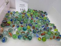 Photo showing a large group of approximately 150 colorful vintage glass marbles piled together, various colors and swirl patterns visible.