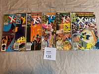 Top view of six vintage Marvel X-Men comic books in protective sleeves arranged side by side on a beige surface. Covers show various characters and action scenes typical for Bronze Age comics.