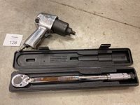 Impact wrench and torque wrench in case, displayed on floor.