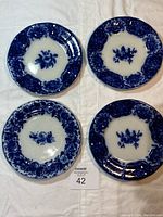 Four blue and white floral display plates laid out, showing detailed patterns and condition overall.