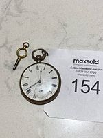 Photo of antique pocket watch with visible cracked glass dial and separate winding key.