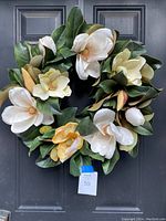 Front view of the artificial magnolia wreath hanging on a black door.