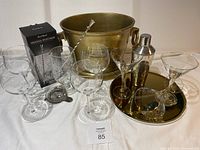 Full display of assorted barware including glassware, brass bucket, mixing pitcher, shaker, tray, and strainer.