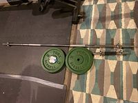 Full layout showing barbell bar, weight plates, dumbbell bar and collars on floor mats and rug.