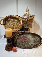 Overall view of all items in the lot: three wicker baskets, antique floral tray, ceramic candle pedestal, pillar candle and apple for size reference