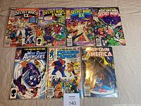 Lot of 7 early 1980s Marvel comics shown together on fabric background including multiple Secret Wars, West Coast Avengers, Squadron Supreme, Captain America titles.