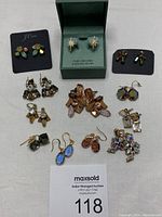 Overview of all 8 pairs of J.Crew earrings in various shapes and colors arranged on a surface with one pair in a green box labeled sterling silver cubic zirconia.