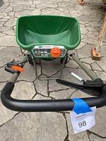 Front angle view showing green hopper, orange control knob, and black handlebar with an orange lever.