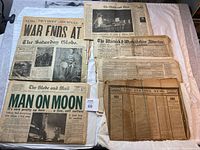 Top view of six historical newspapers with prominent headlines including the 1969 moon landing and WWI end notice.