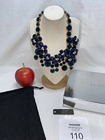 Full view of J Crew chunky blue floral motif statement bib necklace displayed on white bust with apple for scale, original box and dust bag included.