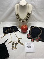 Three J Crew statement necklaces on display with dust bags and apple for size reference