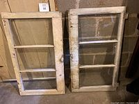 Pair of vintage wooden window frames from a 1946 house side by side on the floor, showing aged paint and glass panes.