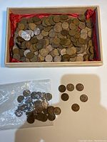 Wooden box filled with a large quantity of copper pennies showing wear and age patina, some pennies placed outside in plastic bag and loose on table.
