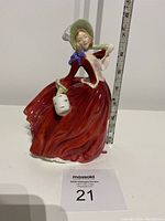 Front view of Royal Doulton Autumn Breezes porcelain figurine, showing the woman in flowing red dress and bonnet with white handbag, approx. 9 inches tall.