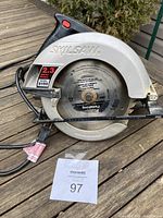 Side view of Skilsaw circular saw on wooden surface showing body and blade guard.