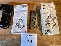 SOG Paratool multi-tool closed with original leather sheath, instruction manual, and box displayed on wooden surface.