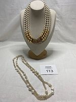 Both necklaces displayed together on fabric with one on a bust form showing the retro multi-strand necklace.