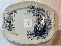 Full view of off-white ceramic platter with grey-black floral and bumblebee design and scalloped edges.