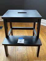 Front view of the black wooden step stool showing two steps and rectangular design.