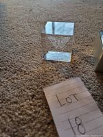 Small cube glass paperweight with etched butterfly and chip on corner, placed on carpet with reflection visible