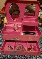 Open pink Barbie music box showing rotating Barbie figurine in pink dress, mirror, compartments, and costume jewelry inside.