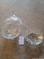 Two clear glass candy dishes placed on carpet, one with lid and one open on pedestal base with feet, showing detailed cut-glass pattern.