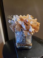 Artificial beige hydrangea centerpiece in a square glass vase with clear glass pebbles inside.